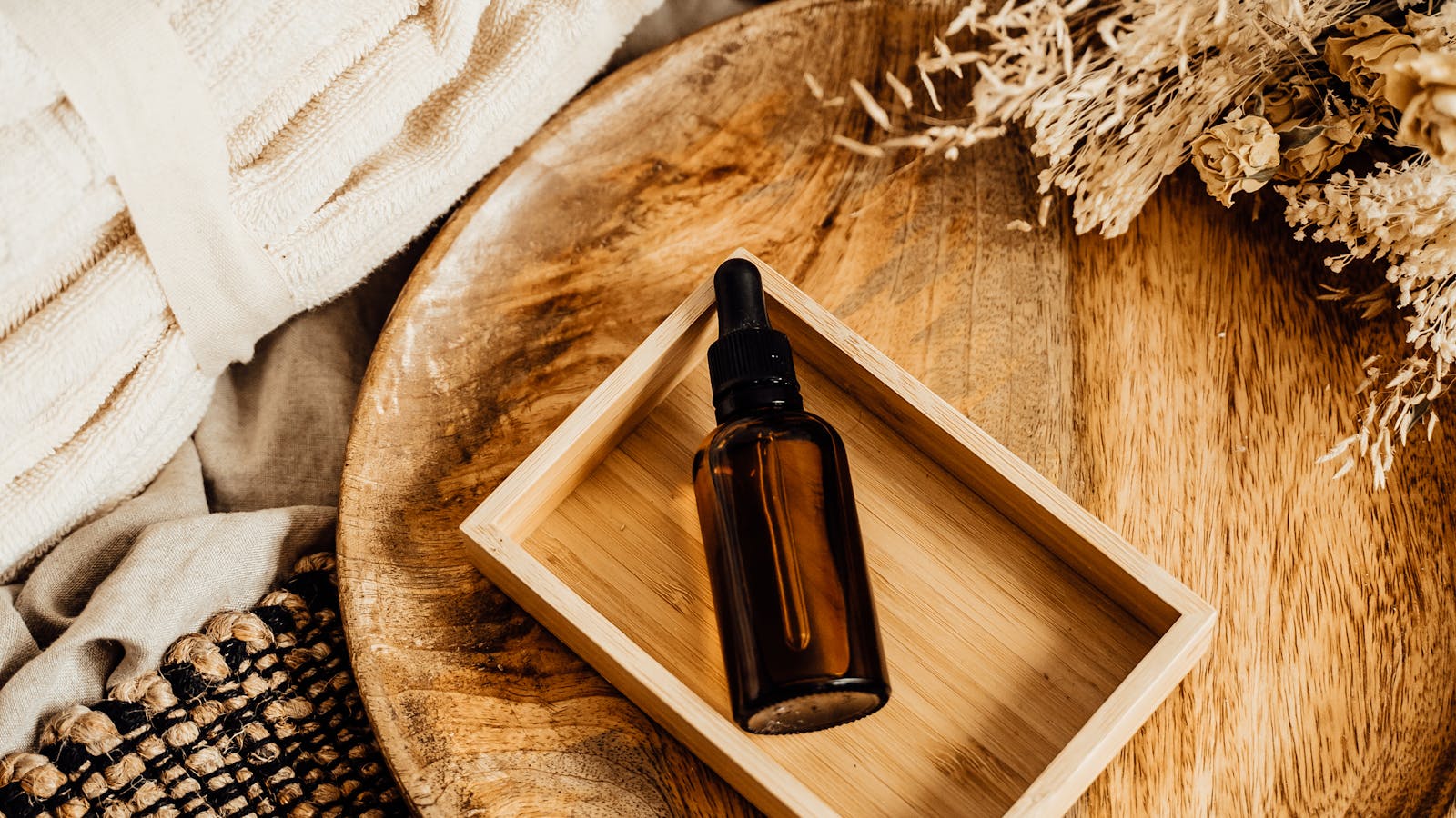 Botella de aceite esencial en bandeja de madera con flores secas